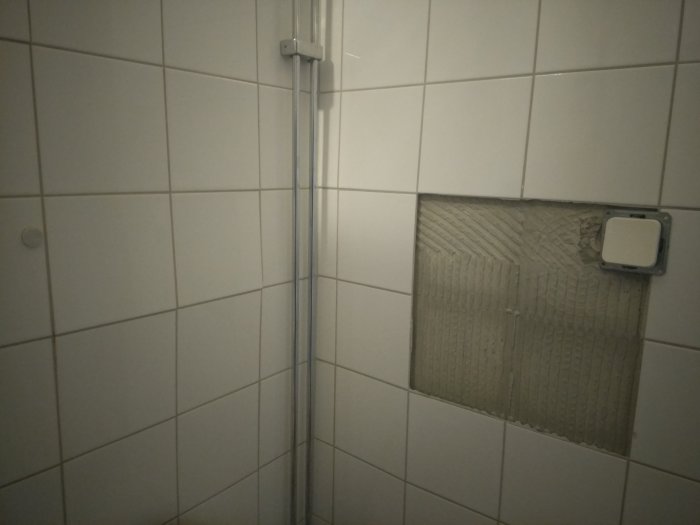 Kakelplattor saknas ovanför en strömbrytare, exponerat väggunderlag med spackel och kakel i badrum.