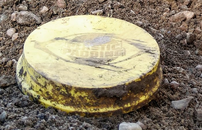 Gult lock från Plastic Padding-burk som täcker änden på ett dräneringsrör i jord.