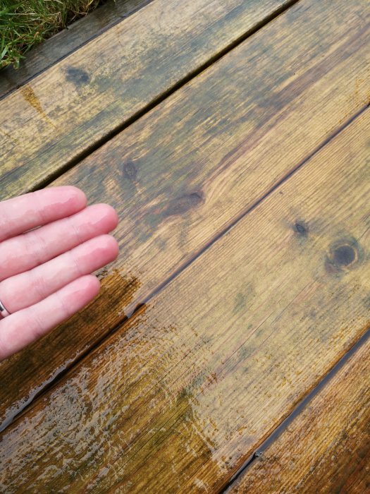 Trädäck med missfärgningar och hand som pekar ut fläckar efter användning av trallrent.