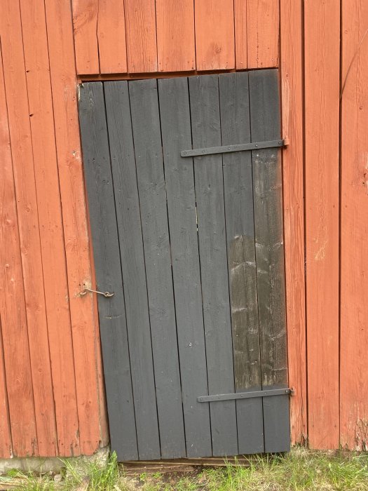 Sned svart dörr med slitna kanter på en röd trävägg.