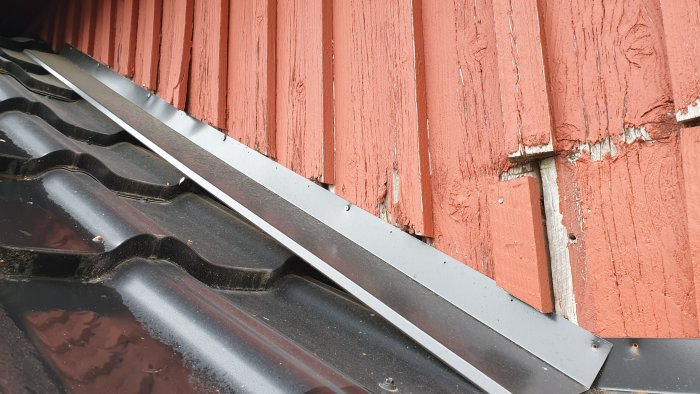 Dåligt installerad hängränna och vindskiveplåt mot slitet rött trähus, synliga skruvar, utan överlapp.