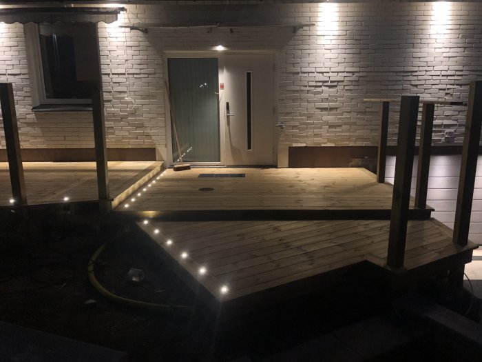 Nybyggd trätrall med LED-belysning runt om på kvällen och två trappsteg synliga.
