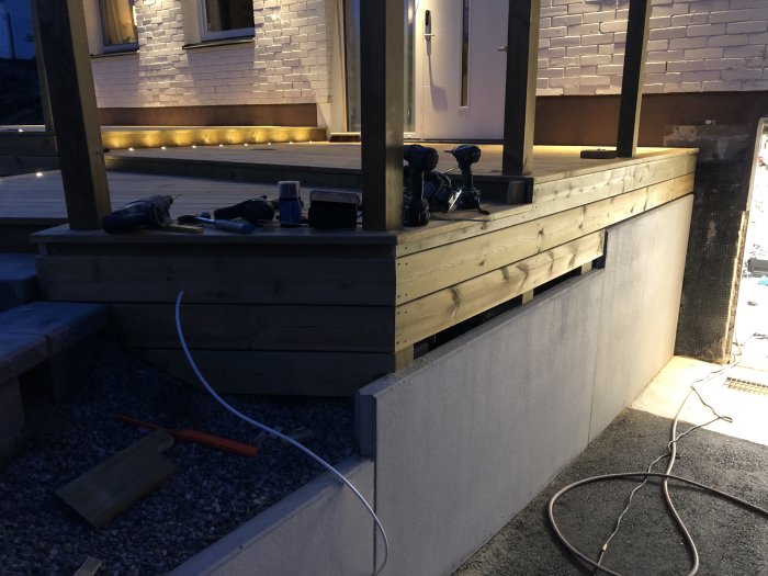 Nästan färdigställd trall med spotlights och verktyg på steg under kvällsbelysning.