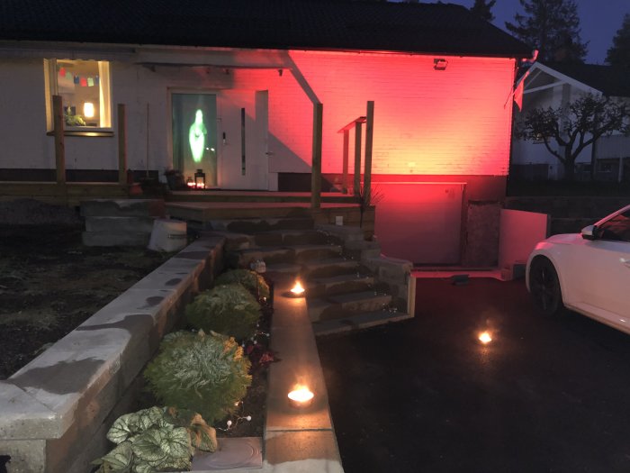 Husfasad med röd belysning och en projicerad bild av ett spöke i fönstret, dekorerat för Halloween.