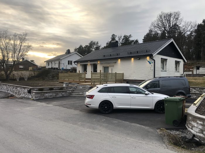 Ett vitt enplanshus med nytt trästaket och svensk flagga, samt en barngrind synlig på verandan.