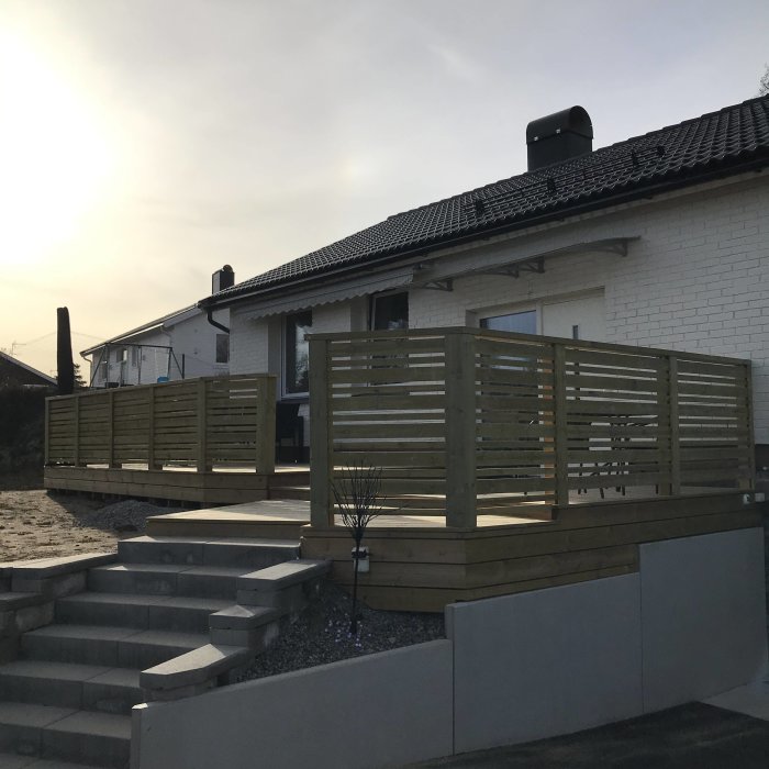 Nybyggd träaltan med säkerhetsräcke och barngrind vid en vitputsad villa under solig himmel.