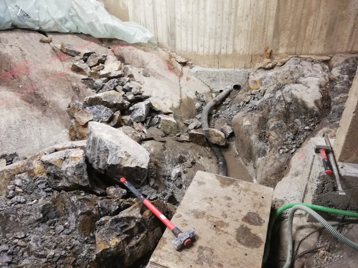 Sten och makadam i källardike med verktyg för spräckning av stenar.