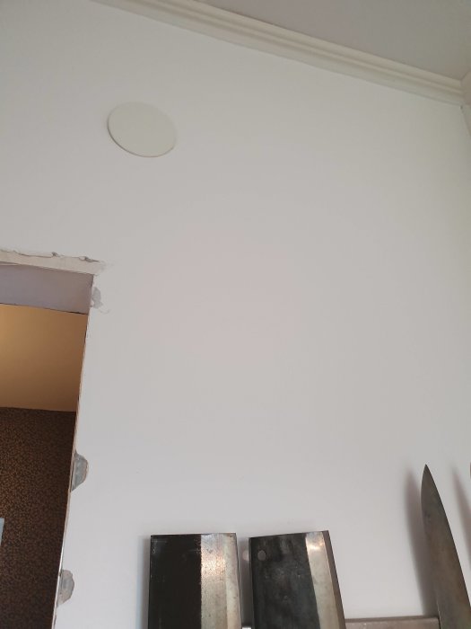 Vägg med borttagen dörröppning och synliga reglar, kökets strömbrytare nära kanten, rund detektor ovanför.