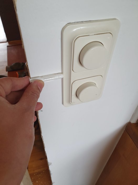 Hand som håller en vit plugg vid sidan av en dubbel ljusströmbrytare monterad på en vit vägg.