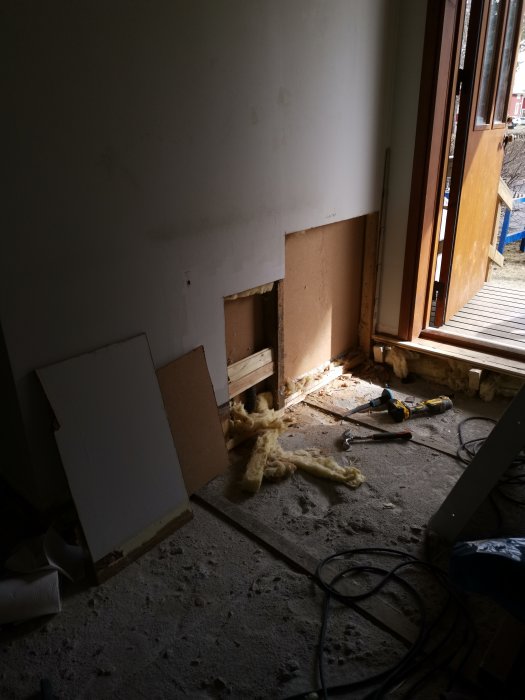 Renoveringsarbete vid vägg nära öppet fönster med synlig isolering och verktyg på golvet.