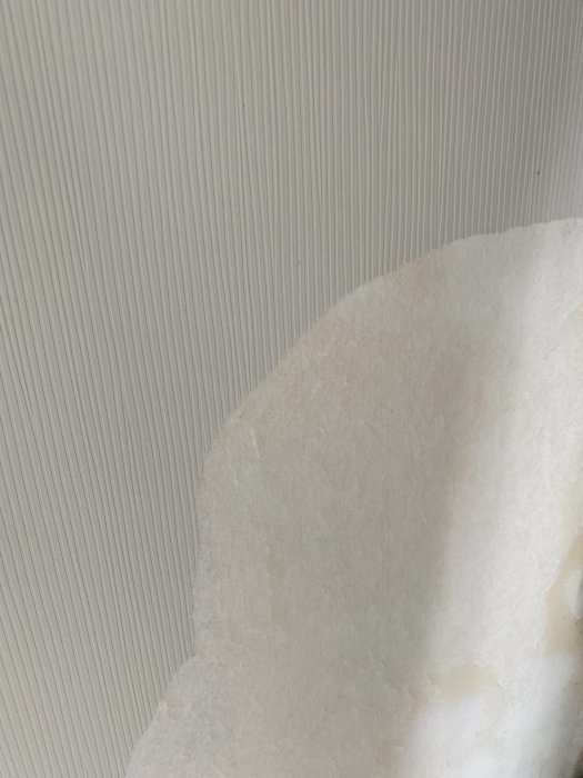 Texturerad tapet med hård yta där en del är bortriven och visar underliggande lager.