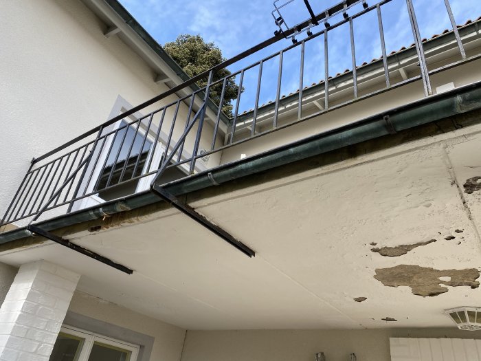 Bild av en balkong med slitet räcke och flagnad färg på betongundertaket som behöver underhåll.
