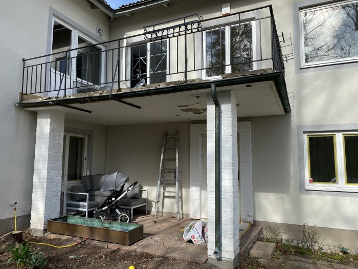 Balkong i behov av underhåll med slitet räcke och flagnande färg på kant på vitputsat hus.