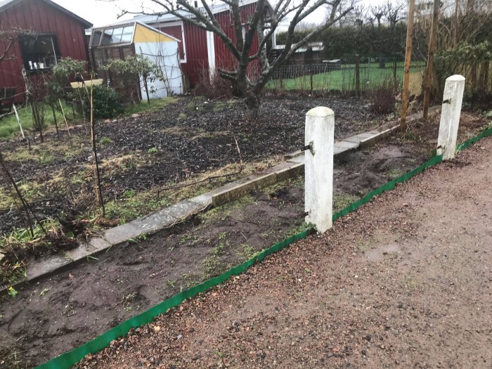 Delvis nedfallen staketsektion i koloniområde med skadade plankor och betongpelare.