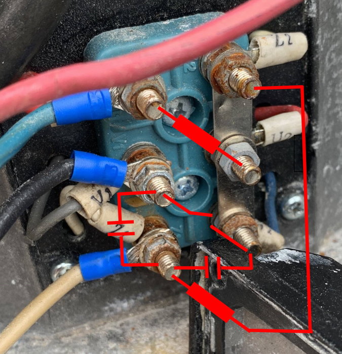 Närbild på en elektrisk kopplingsplint med påfrestade lindningar och en brytare, markerade med röda pilar.