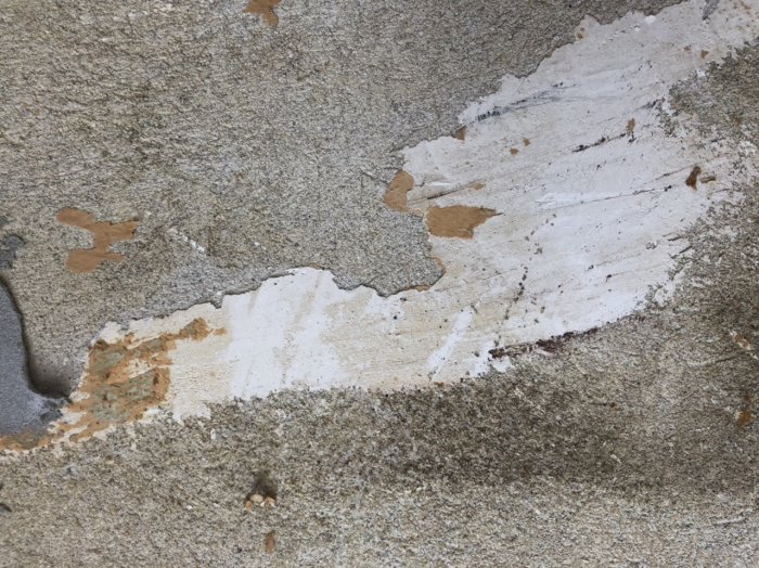 Betongvägg med rester av vit spackel och avskrapade tapetlager.