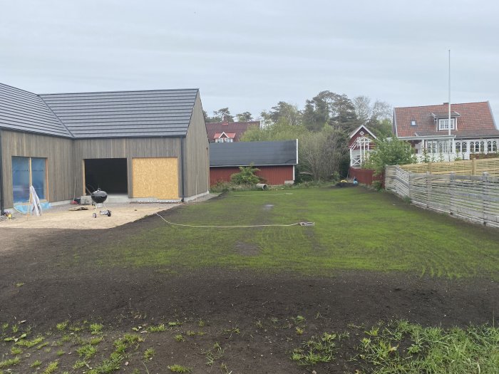 Nyplanterad gräsmatta framför byggplats med pågående konstruktion av carport och förråd.