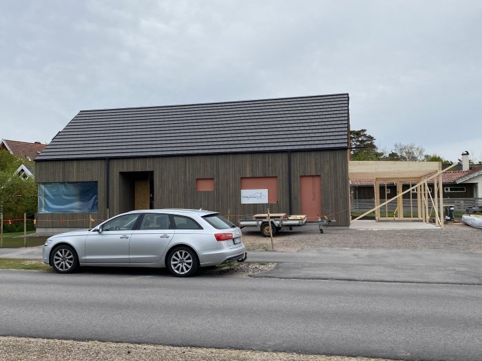 Hus under renovering med nytt tak, en bil framför, och en nyligen påbörjad träkonstruktion för carport.