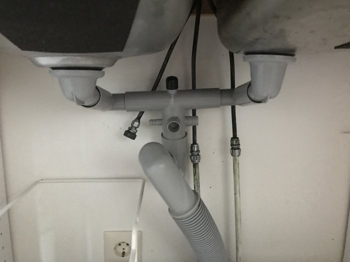 Undersidan av ett köksskåp med vaskavlopp, vattenkrananslutningar och eluttag, utan ballofix för diskmaskin.