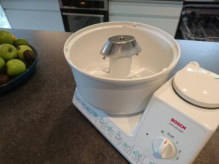 En Bosch köksmaskin på ett köksbord, med en skål gröna äpplen i bakgrunden.