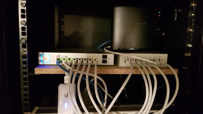 Nätverksutrustning i skåp med patchpanel, modem, switch och anslutna kablar.