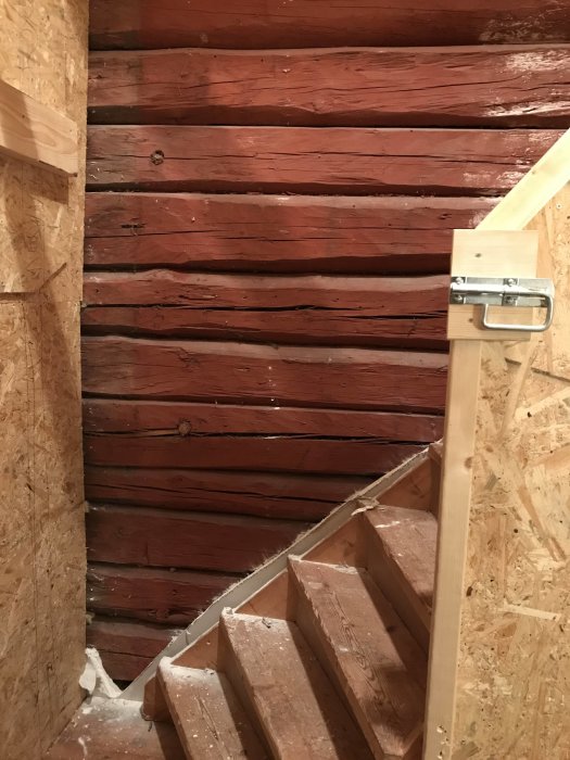 Trappsteg i trä med rödmålade stockväggar och OSB-skivor, indikerar förberedelse för renovering.