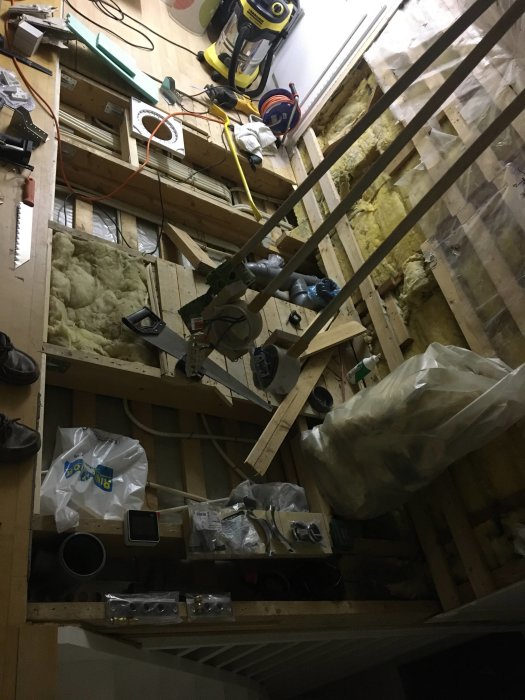 Rivna golvbjälkar med synlig isolering, verktyg och golvbrunn i en pågående renovering.