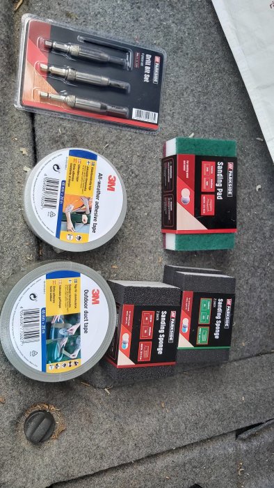 Byggverktyg och -material: mejslar, silvertejp, och slipmaterial på betongunderlag.