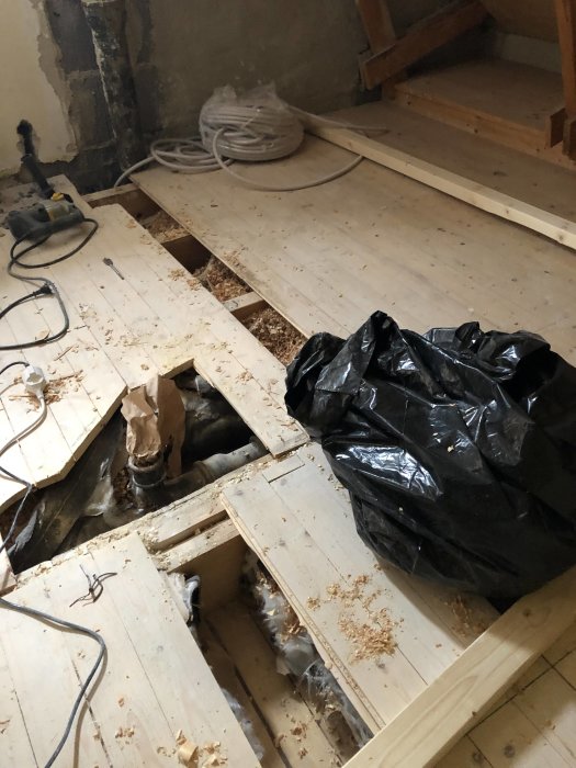 Delvis avtäckt bjälklag med synliga bjälkar och elinstallation, samt en öppning i golvet.