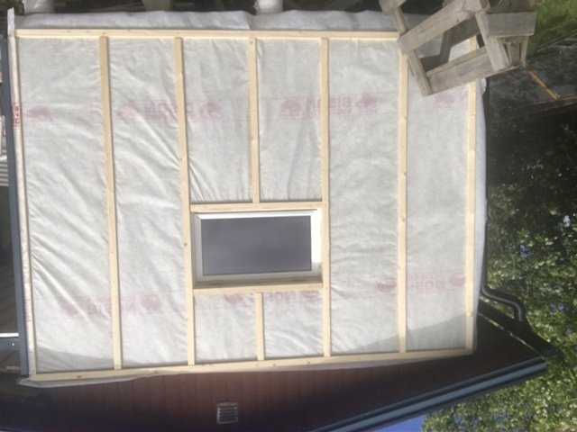 Vägg med isolering och reglar redo för panel, litet fönster i mitten.