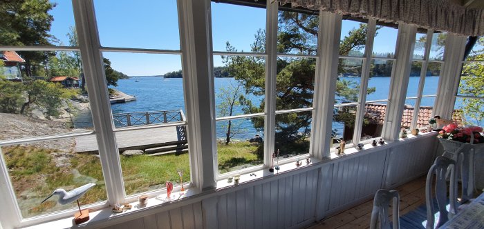 Utsikt från en glasveranda med spröjsade fönster i ett äldre hus, med utsikt över lugnt vatten och brygga i Stockholms skärgård.