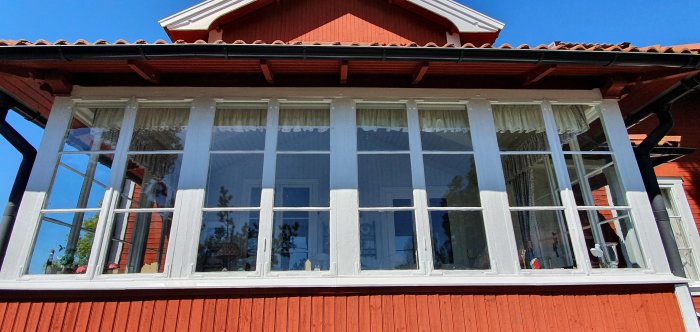 Ett gammalt spröjsat fönsterparti på en glasveranda till ett rött sommarhus, som visar tecken på mångårig användning.