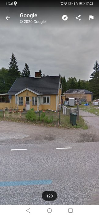 Gul husfasad med svart tak, behöver renovering, oordnad gård med olika föremål och byggmaterial.