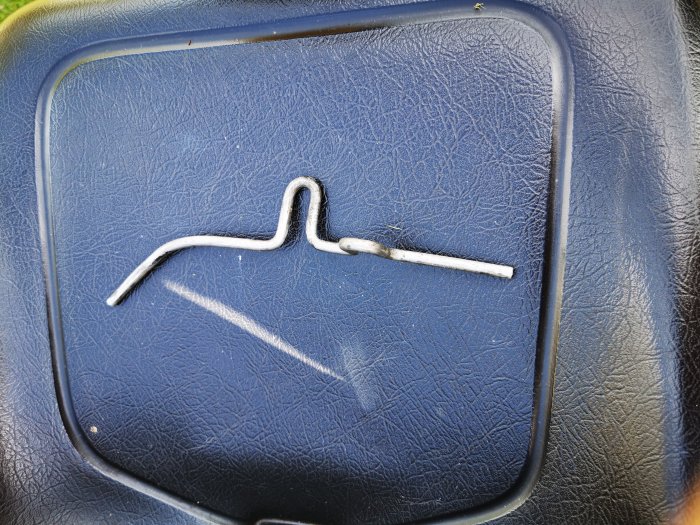 Bent metal component lying on a textured blue surface, possibly from a ride-on mower.