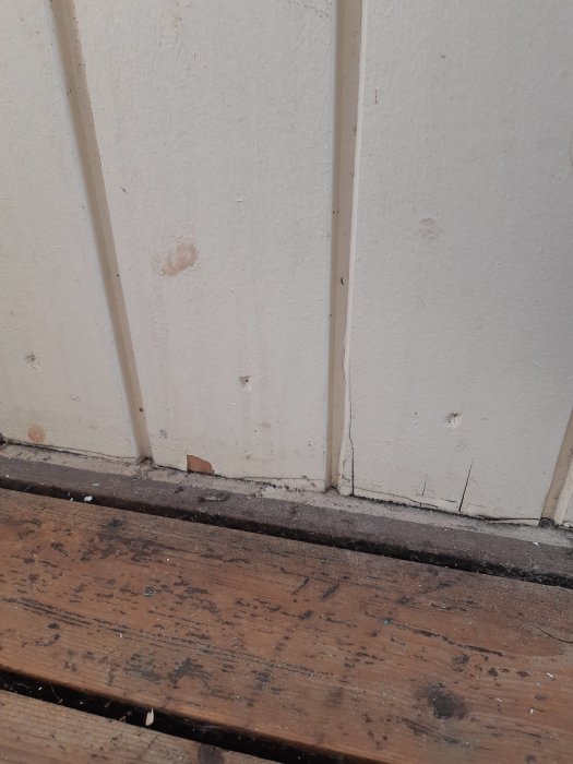 Väggpanel an mot trägolv utan luftspalt på en veranda som ska renoveras.