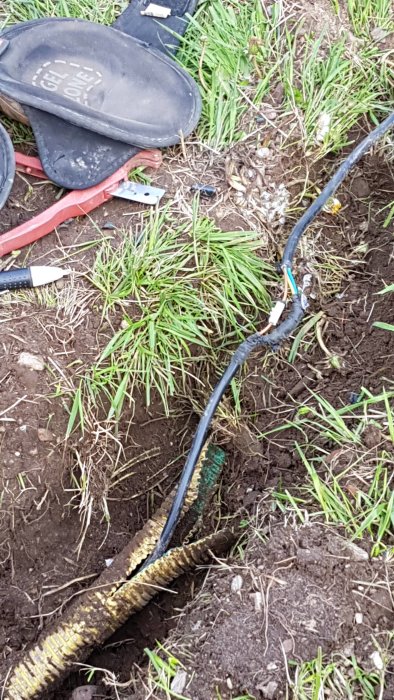 Elektrisk kabel med improviserad sockerbitskoppling i grävd grop, omslutet av svart tejp.