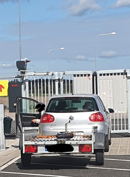 Bil med släp lastat med byggmaterial, inklusive reglar och takplast, säkrade med spännband och kudde.