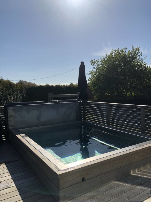 Uppvärmd utomhuspool på trädäck med soligt väder och blå himmel i bakgrunden.