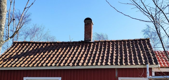 Tak med röda tegelpannor på en byggnad med en tegelskorsten, synliga svackor och ojämnheter i takstrukturen.