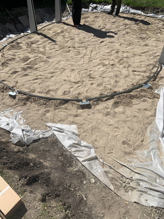 Rund betongplatta under anläggning med bottenarmering som ligger på ett jämnt underlag av sand, byggplats i dagsljus.