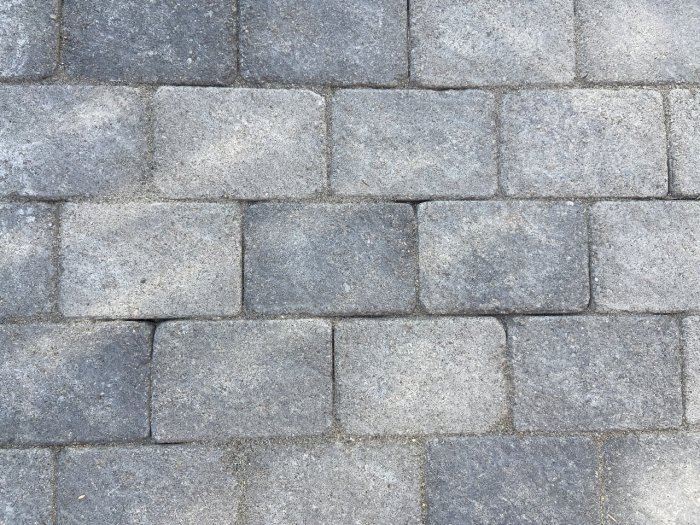 Stenläggning med grå marksten där några stenar har lossnat och skapat glapp efter användning av lövblåsare.