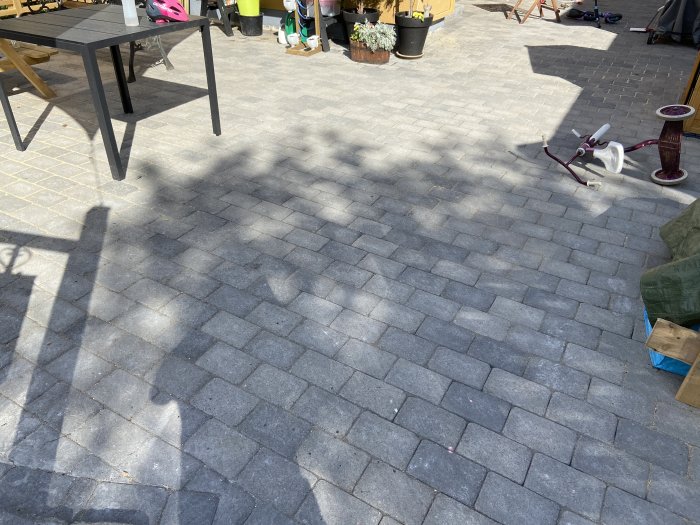 Stenläggning som visar tecken på skador efter användning av lövblåsare, med trädgårdsredskap i bakgrunden.