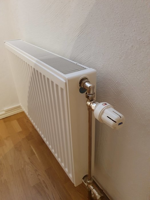 Vit radiator med termostat i ett hörn av ett rum, troligen inköpt för cirka 10 år sedan.