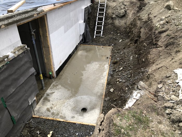 Nyligen gjuten betongplatta för källarnedgång täckt med plast vid en byggarbetsplats.