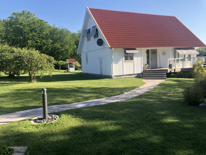 Välskött trädgård med grönt gräs, vit villa och stenlagd gångväg.