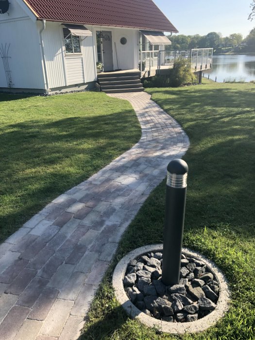 Välhållen trädgård med en slingrande stenlagd gångväg och välskött gräsmatta framför ett hus.