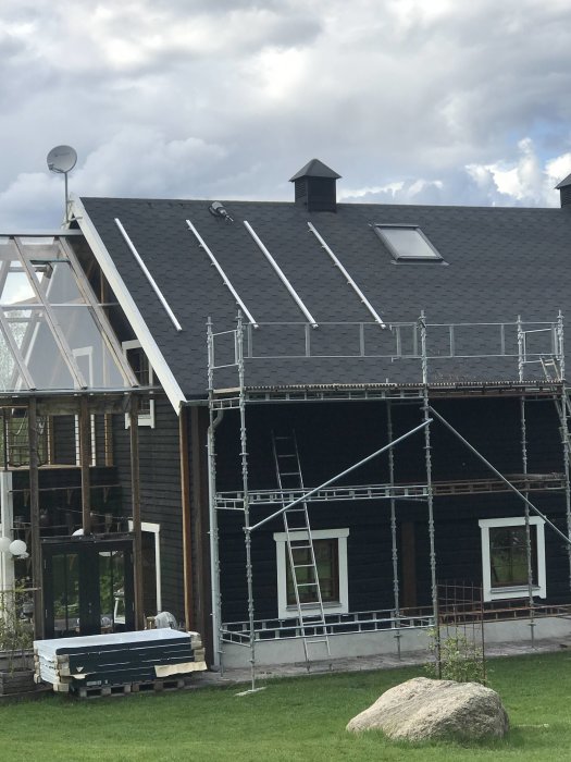 Solfångare installerade på taket av ett hus med svart träfasad, omgivet av byggnadsställningar.