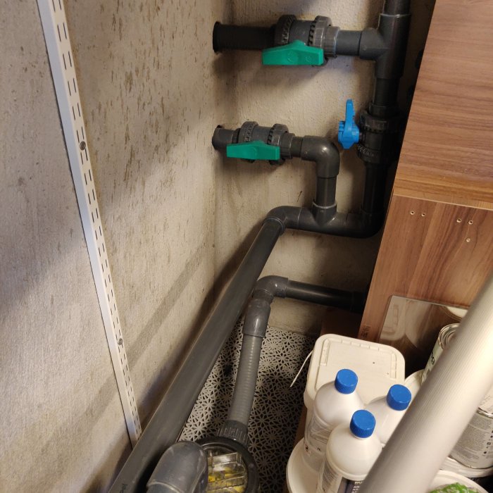 Rörinstallation med gröna ventiler och blå pump i ett tekniskt utrymme.