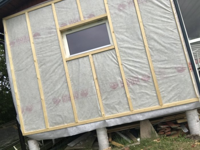 Vägg under renovering med tilläggsisolering och monterade reglar för luftspalt på en sommarstuga.