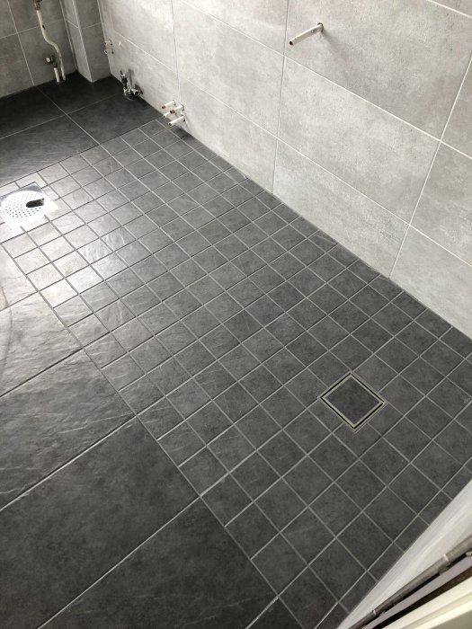 Nylagda klinkerplattor i badrum med små och stora plattor samt duschbrunn.